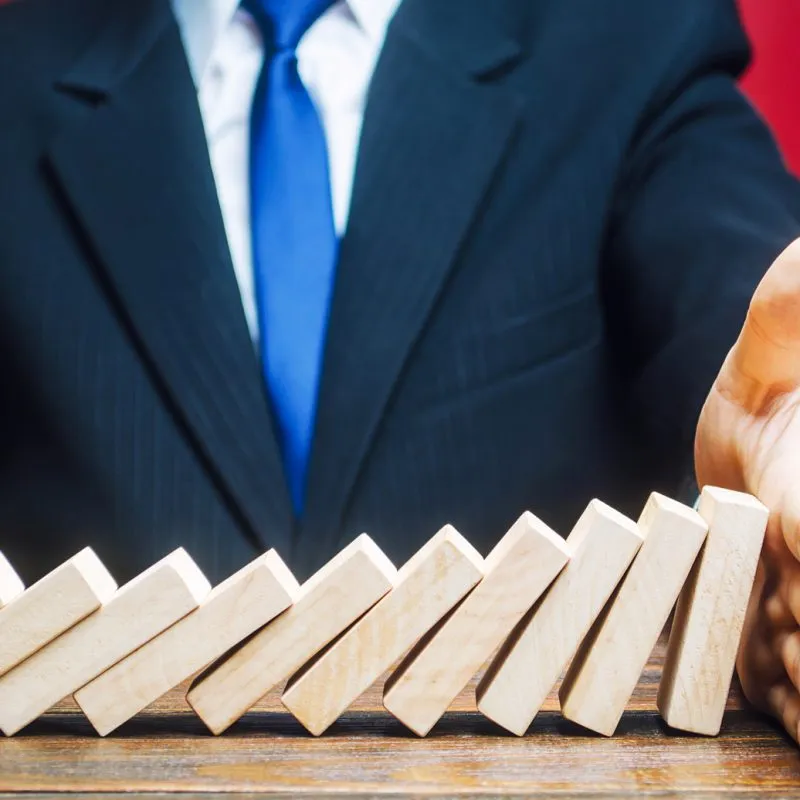 businessman stops domino falling with his palm risk management concept